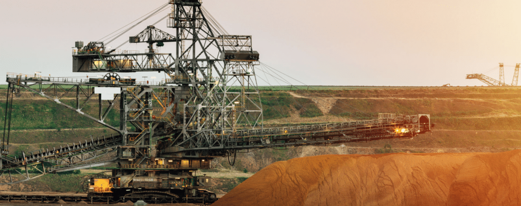 Large industrial mining machine excavating earth at an open-pit mine, with piles of soil and terraced landscape in the background.
