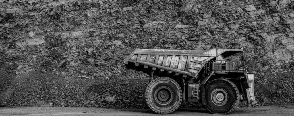 A large mining dump truck parked in front of a rocky, layered quarry wall.