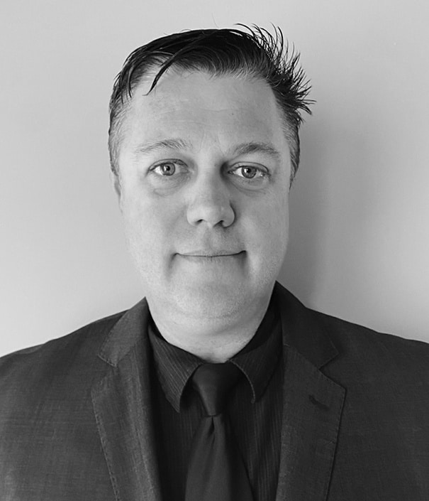 A man wearing a suit and tie poses for a black-and-white portrait against a plain background.