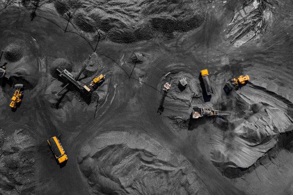Aerial view of heavy machinery and trucks operating in a large open-pit mining site, moving and processing dark earth and minerals.